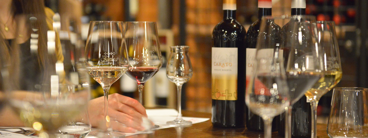 Calici Delea con vino bianco e rosso e bottiglie di Carato sul tavolo di degustazione